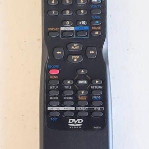 May include: Black DVD remote control with multiple buttons for power, playback, and menu navigation. Features buttons for numbers, volume, and channel control. Includes text: DVD, VIDEO, and NA270.