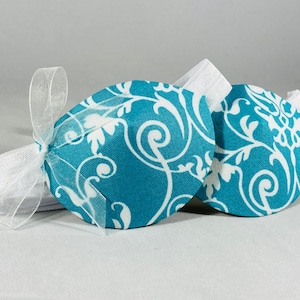 May include: Two teal blue fabric eye masks with a white floral pattern. The masks are tied together with a white ribbon.