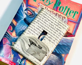 May include: A Harry Potter and the Prisoner of Azkaban book with a handmade bookmark featuring a white owl with a letter in its beak. The bookmark is made of paper and has a glittery finish.