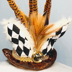 May include: A brown top hat with a black and white checkered band, gold trim, and a pocket watch with the words "I'm Late" on the face. The hat is decorated with brown and white feathers.