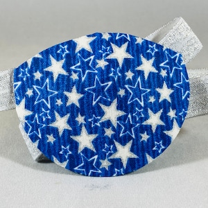 Può includere: Un cerotto per l'occhio blu con un motivo a stelle bianche. Il cerotto per l'occhio è attaccato a un elastico bianco.