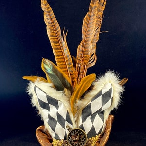 May include: A whimsical hat with a black and white checkered pattern, brown fur trim, and a gold clock and chain. The hat is topped with brown and gold feathers.