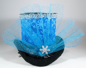 May include: A blue top hat with a snowflake design and a white lace trim. The hat is decorated with a blue tulle bow and a silver snowflake.