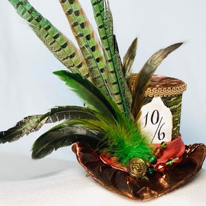 May include: A green and brown top hat with a 10/6 tag, decorated with green and brown feathers and a red ribbon.