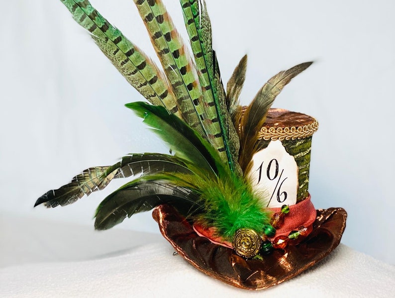 May include: A green and brown top hat with a 10/6 tag, decorated with green and brown feathers and a red ribbon.