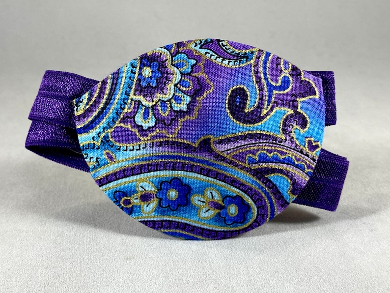 Pode incluir: Atadura para olho de paisley roxo e azul com uma faixa el&aacute;stica roxa.