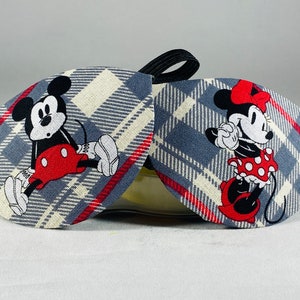May include: A pair of sleep masks with a plaid pattern in grey, white, and red. One mask features Mickey Mouse and the other features Minnie Mouse.