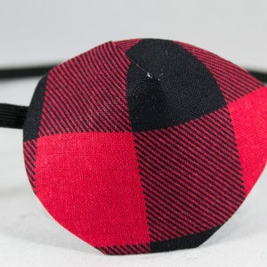 May include: Red and black plaid eye patch with an elastic strap.