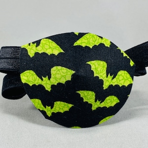 May include: Black eye patch with an elastic strap. The patch is decorated with a repeating pattern of green bats on a black background.