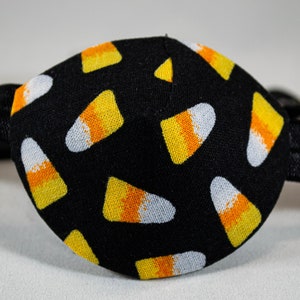 May include: Black eye patch with a pattern of yellow and orange candy corn on a white background.