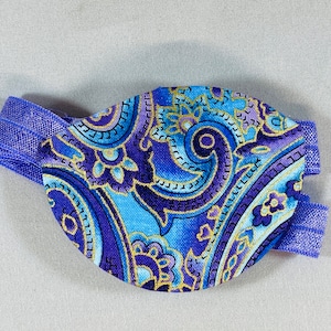 Pode incluir: Um tapa-olho azul e roxo com padr&atilde;o paisley e uma faixa el&aacute;stica azul.