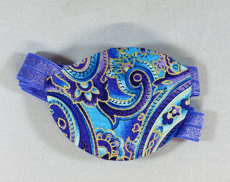 Pode incluir: Um tapa-olho azul e roxo com padr&atilde;o paisley e uma faixa el&aacute;stica azul.