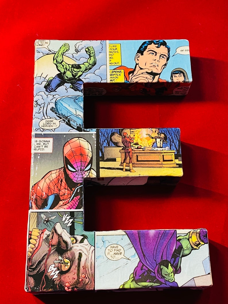 Op de afbeelding: Een grote letter E gemaakt van karton bedekt met comicboekpagina's met superhelden zoals Hulk, Superman en Spiderman. De letter staat op een felrode achtergrond.