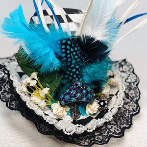 May include: A black and white checkered top hat with blue and white feathers, white flowers, and a jeweled mushroom accent. The hat is trimmed with black lace.
