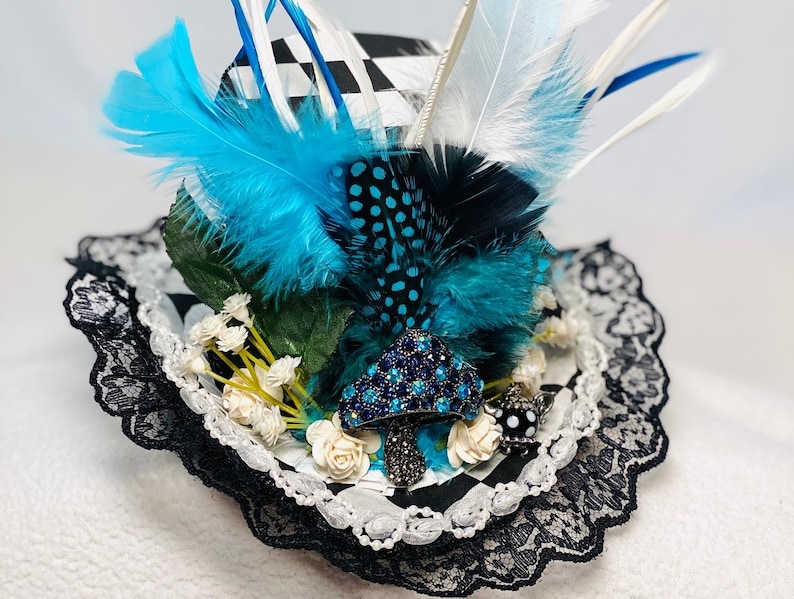 May include: A black and white checkered top hat with blue and white feathers, white flowers, and a jeweled mushroom accent. The hat is trimmed with black lace.