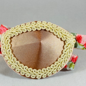 May include: A brown eye patch with a decorative gold trim. The eye patch is attached to a floral patterned elastic band.