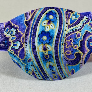 Pode incluir: Atadura para olho em paisley roxo e azul com acabamento dourado e faixa el&aacute;stica.