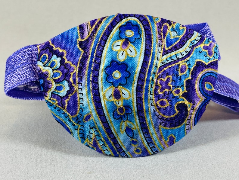 Pode incluir: Atadura para olho em paisley roxo e azul com acabamento dourado e faixa el&aacute;stica.