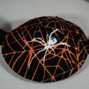 May include: Black eye patch with an orange spider web design and a white spider in the center.