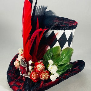 May include: A black and white checkered top hat with red and black feathers, red roses, and white flowers. The hat has a red and black lace trim.
