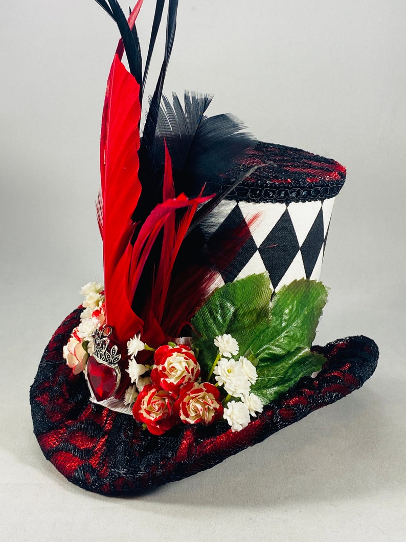 May include: A black and white checkered top hat with red and black feathers, red roses, and white flowers. The hat has a red and black lace trim.