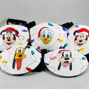 May include: Five eye patches featuring various Disney characters wearing Santa hats. The characters are Mickey Mouse, Minnie Mouse, Donald Duck, Goofy, and Pluto. The background of the eye patches is white with colourful Christmas lights.
