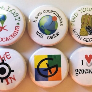 May include: Six round white buttons with different designs related to geocaching. The buttons feature text such as "I'm not lost, I'm geocaching", "Find yourself with geocaching", "Cache in", and "I love geocaching".