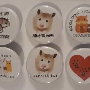 May include: Six round white buttons with images and text about hamsters. The buttons feature images of hamsters, hearts, and paw prints. The text on the buttons includes "I love my hamsters", "Hamster Mom", "Big or small I love them all", "Home is where the hamsters are", "Hamster Dad", and "I love my hamsters".