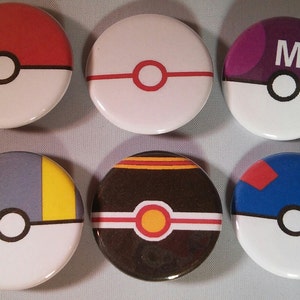 May include: Six round, white, button-style pins with different colored designs. Each pin features a black outline of a Pokeball with a white center circle. The designs include red, white, and black; red, white, and orange; purple with the letter "M"; gray, yellow, and white; black, orange, and white; and blue, red, and white.
