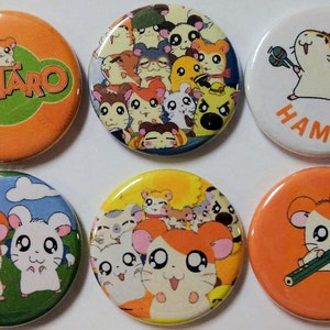 May include: Six round orange, white, and blue buttons with cartoon hamsters from the anime Hamtaro. The buttons feature different images of the hamsters, including Hamtaro playing the maracas, Hamtaro with a pencil, and a group of hamsters.