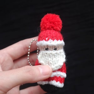 Peut inclure: Petit ornement de Père Noël tricoté, avec un bonnet et un costume rouges, une barbe blanche et des bottes noires. L'ornement est doté d'une chaîne argentée pour l'accrocher. Décoration de vacances festive.