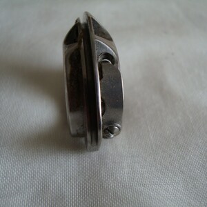 May include: A silver sewing machine bobbin winder with a metal casing and a small screw on the side.