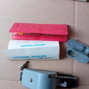 May include: A vintage Y.S. Star automatic zig-zagger sewing machine attachment. The image shows the attachment, a red plastic case, and the original packaging. The packaging includes the text "AUTOMATIC ZIGZAGER" and "MODEL NO. YS-7".