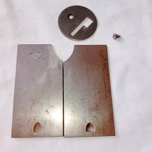May include: Two rectangular metal plates with a dark, weathered finish, each featuring a small semi-circular cutout at the bottom. A circular metal disc with a rectangular slot and a small screw are included. The right plate has the text PATENTED.