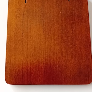 May include: A rectangular wooden sign with a rich, reddish-brown finish. Two black metal hinges are attached to the top edge, with screws visible. The sign has a smooth, polished surface, suggesting it's ready for display.