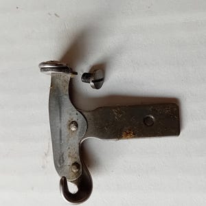 May include: A silver metal sewing machine part with a hook and a small screw. The part is detached from the screw.