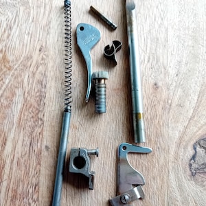 Könnte beinhalten: Eine Sammlung silberfarbener Nähmaschinenersatzteile aus Metall, bestehend aus einer langen Stange mit Spiralfeder, einem Simanco 35020 Hebel, einer kleinen Gewindeschraube, einer Metallklammer, einem dünnen Stift, einem zylindrischen Stab, einer kleinen Klemme mit Schraube und einem Haken.