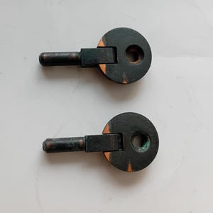 Könnte beinhalten: Zwei antike schwarze Metallscharniere mit kreisförmigem Design und zylindrischem Griff. Die Scharniere haben eine dunkle Oberfläche mit orangefarbenen Akzenten, vor weißem Hintergrund.
