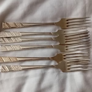Peut inclure: Ensemble de six fourchettes argentées. Les manches présentent un motif répété de lignes diagonales et de motifs floraux. Les dents sont fines, suggérant un service de table formel. Chaque fourchette mesure environ 20 cm de long.