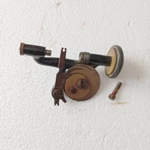 May include: A disassembled antique instrument with a black body, brass accents, and a circular component. The parts include a small screw, a circular brass piece, and a curved black tube. The instrument appears to be a vintage scientific tool.