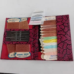 Può includere: Un kit da cucito vintage con una copertina a fantasia floreale rossa e nera. All'interno ci sono rocchetti di filo di vari colori, aghi e filo da rammendo. Il kit include il testo "FINE QUALITY" e "DARNING THREAD MADE IN ENGLAND".