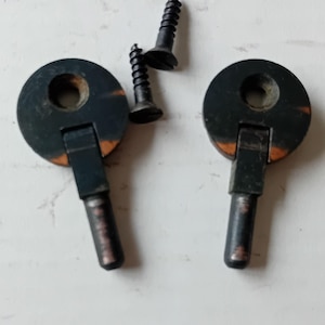 May include: Two black metal cabinet door turn catches with a circular top and a rectangular handle, along with two black screws. The catches have a dark finish with some orange wear marks.