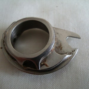 May include: A silver metal sewing machine bobbin winder with a circular opening and a small hook on the side.
