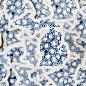 May include: A close-up of a white sticker with a blue outline of the state of Michigan. The outline is filled with a pattern of small circles.