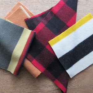 May include: A collection of fabric swatches in various colors and patterns. Includes a gray swatch with yellow and red stripes, a red and black plaid, and a white swatch with black and yellow stripes. Other swatches are tan and brown.