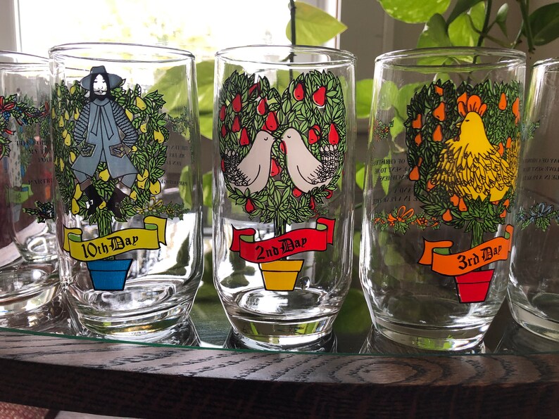 May include: Set of six clear glass tumblers with colorful illustrations of a pear tree, a rooster, and a man. Each glass has a red ribbon with the words "10th Day", "2nd Day", and "3rd Day" printed on it.