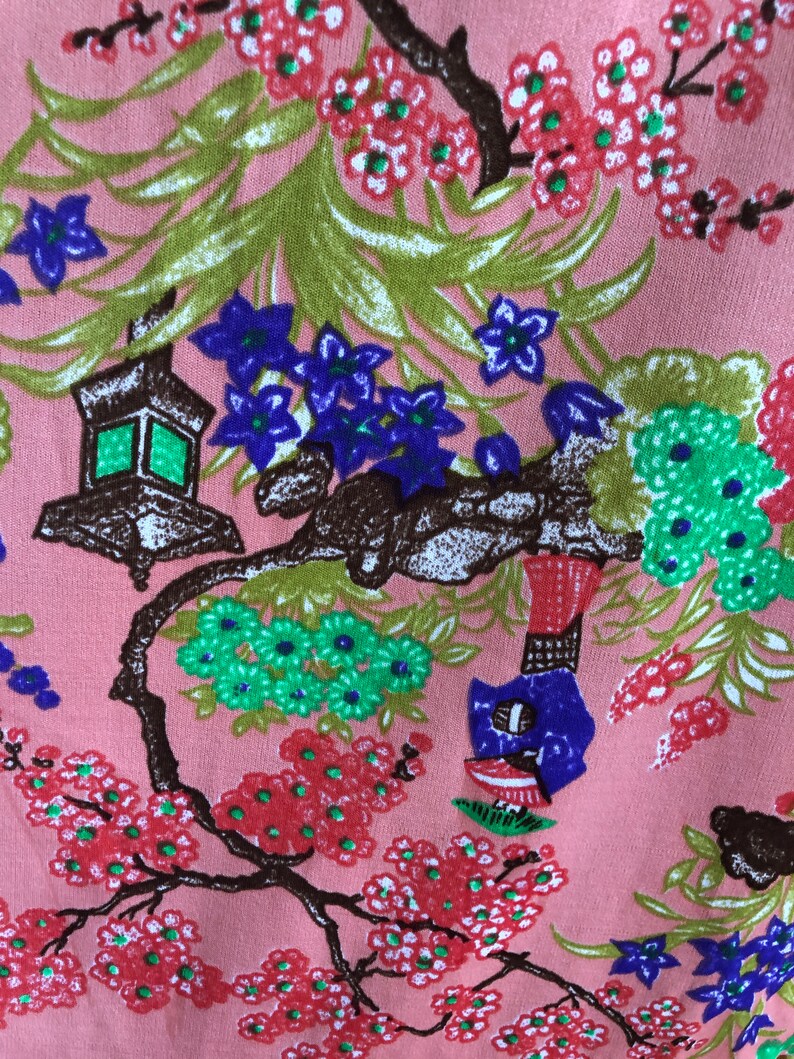 May include: Pink fabric with a floral pattern featuring a brown tree branch with green and blue flowers, a lantern, and a blue bird. The background is a light pink color.
