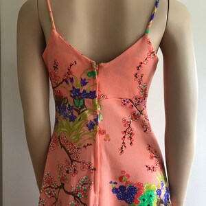 May include: A peach-colored sleeveless dress with a floral print featuring cherry blossoms, birds, and other Asian-inspired motifs. The dress has a V-neckline and a back zipper closure.