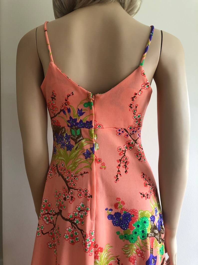 May include: A peach-colored sleeveless dress with a floral print featuring cherry blossoms, birds, and other Asian-inspired motifs. The dress has a V-neckline and a back zipper closure.