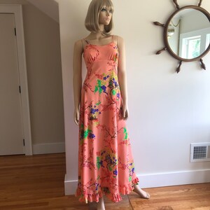 May include: A long, peach-colored maxi dress with a floral print. The dress has thin straps and a ruffled hem.